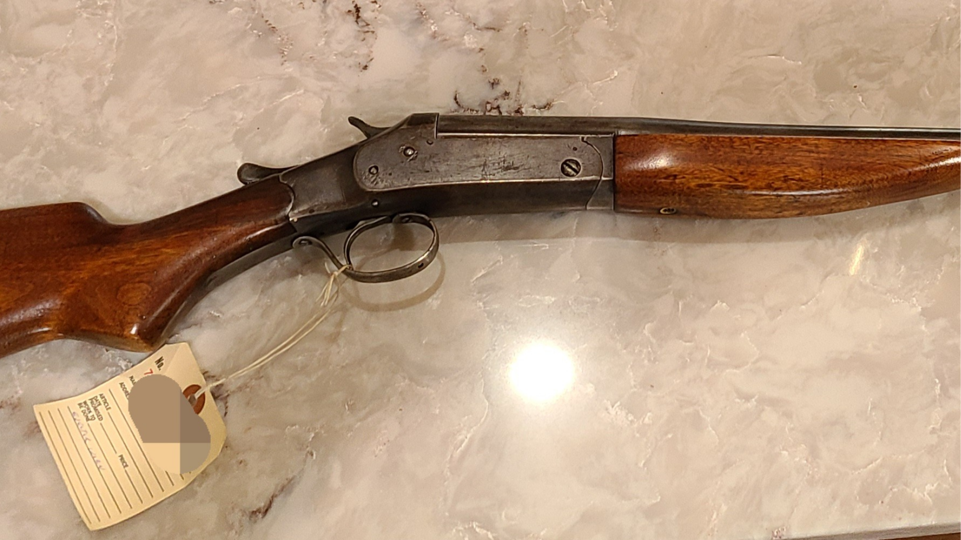 Wooden-stock vintage shotgun with black metal barrel and trigger guard on a marble surface, tag attached