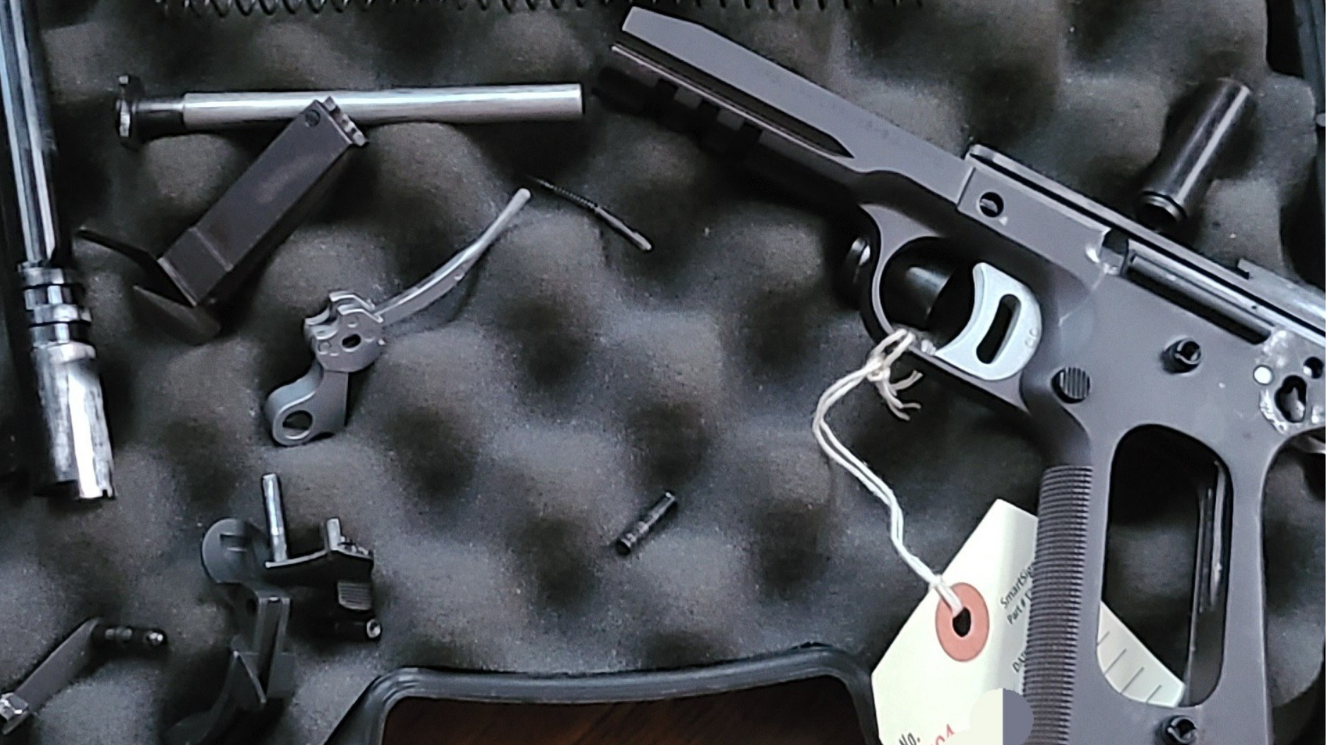 Black metal firearm parts in a foam-lined case, including a receiver, barrel, and accessories.