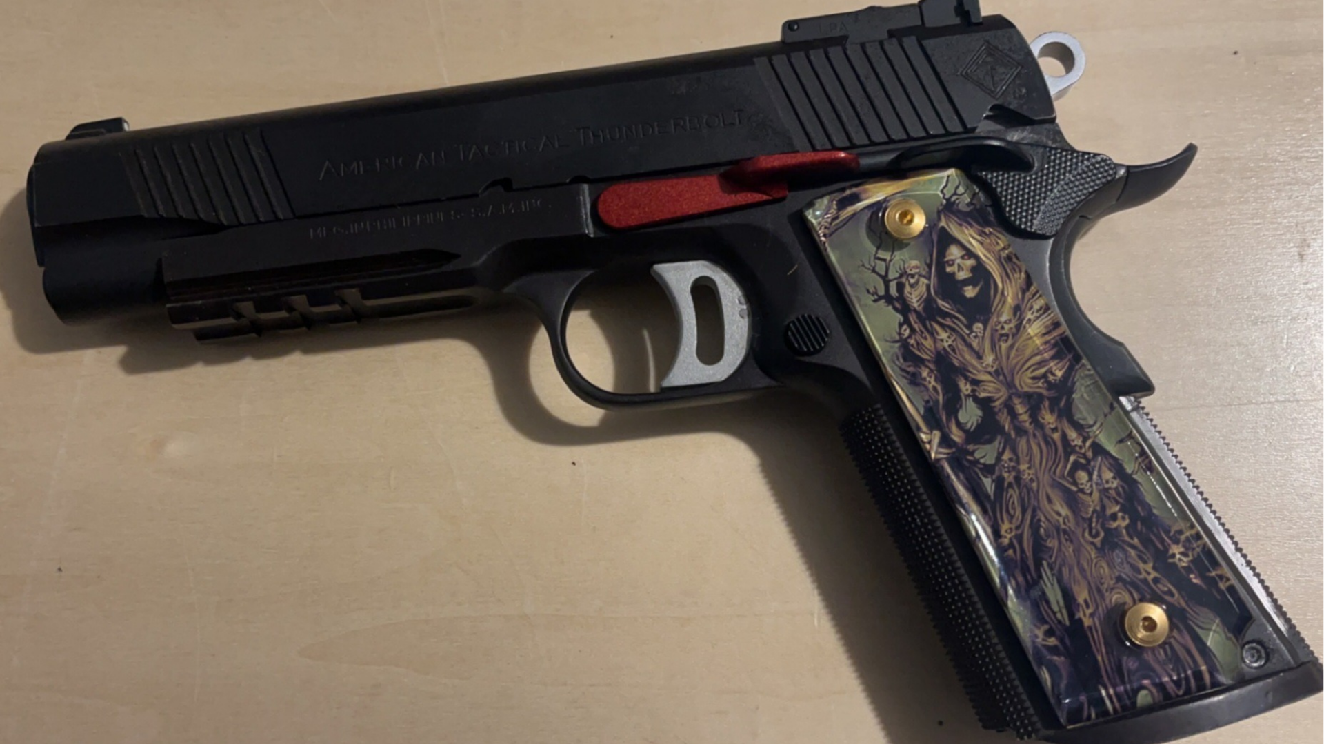 Black semi-automatic handgun with a decorative grip lying on a tan surface