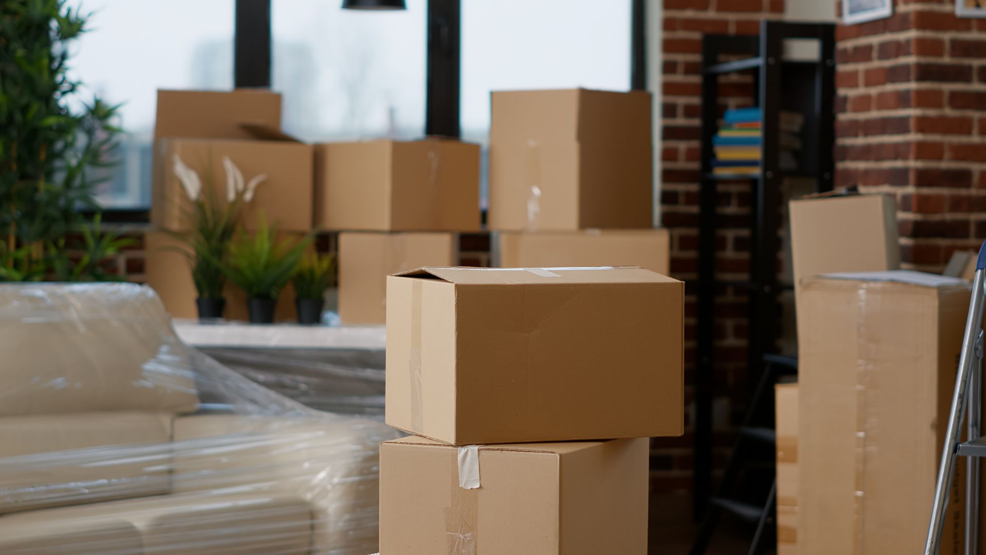 Stacked cardboard moving boxes and a wrapped sofa in an apartment during a move.