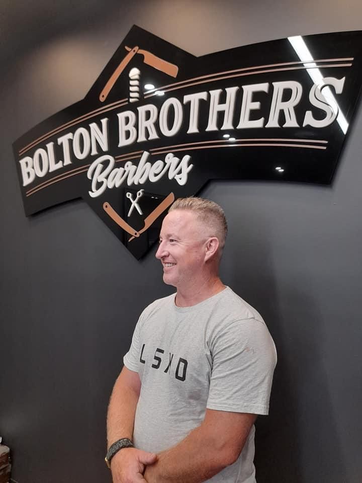 Man With Fresh Haircut Smiling In Front Of Sign — Bolton Brothers Barbers in Erina, NSW