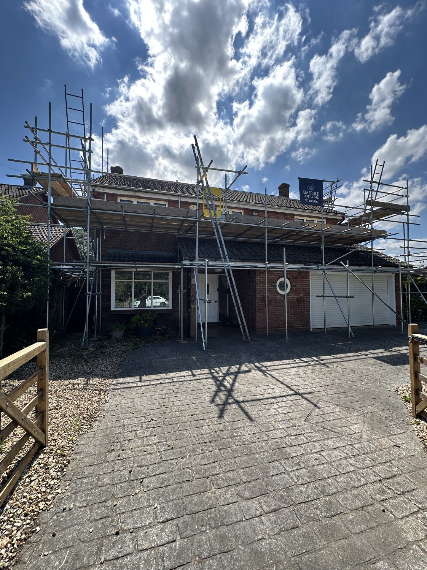 House with scaffolding on roof, parked in driveway under a cloudy sky.
