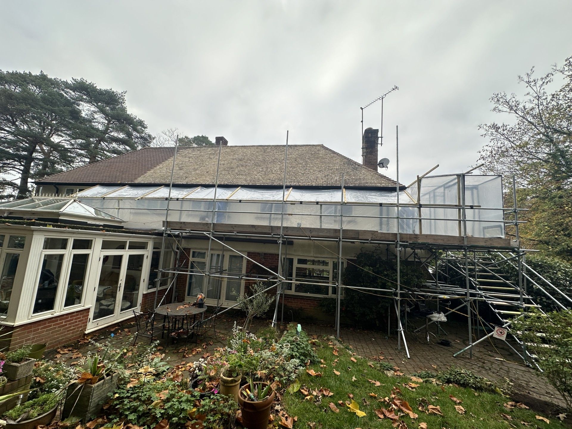 House with scaffolding. Roof partially covered with tarp. Exterior view, cloudy day.