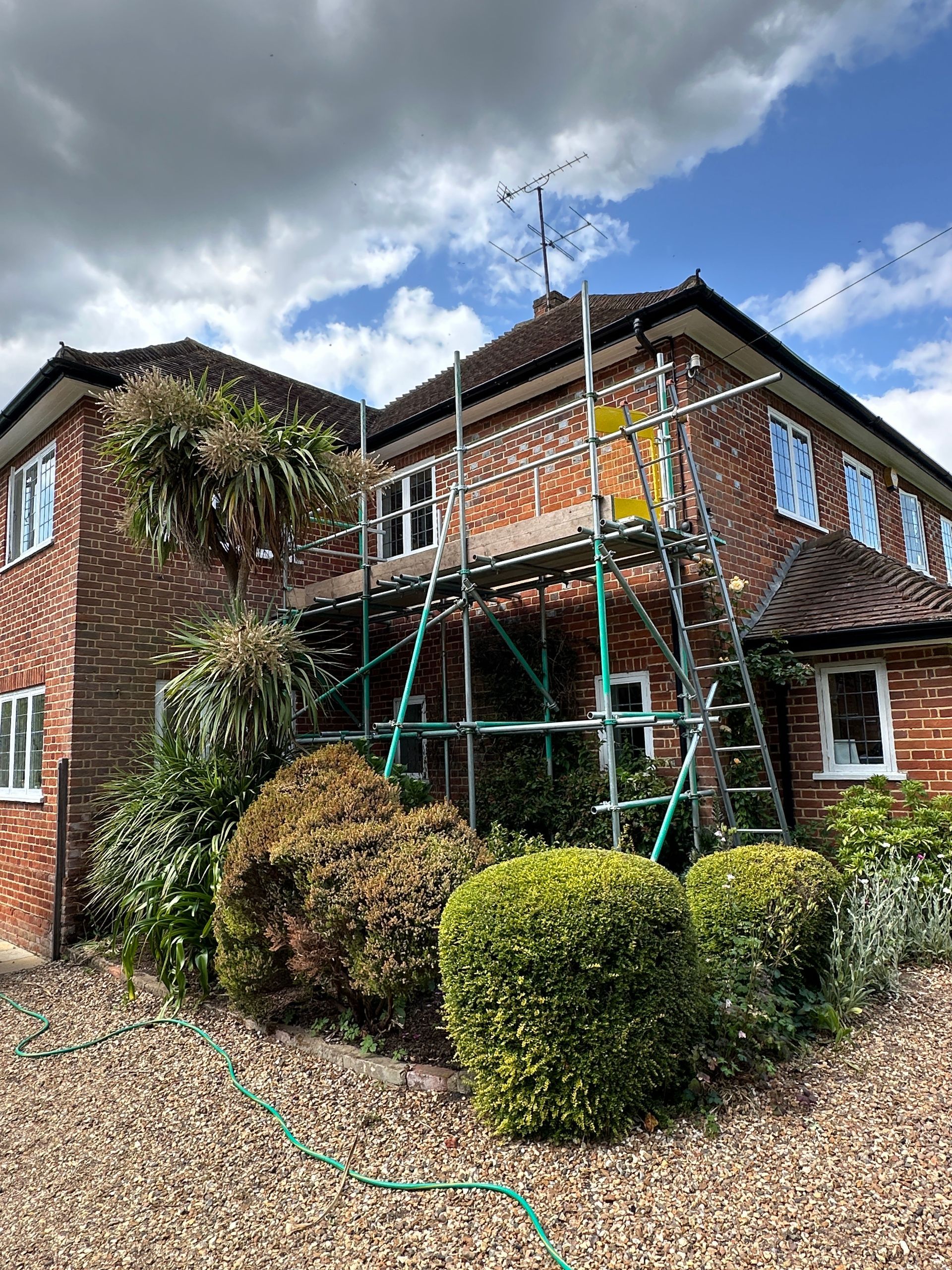 Brick house with scaffolding, garden, and cloudy sky.