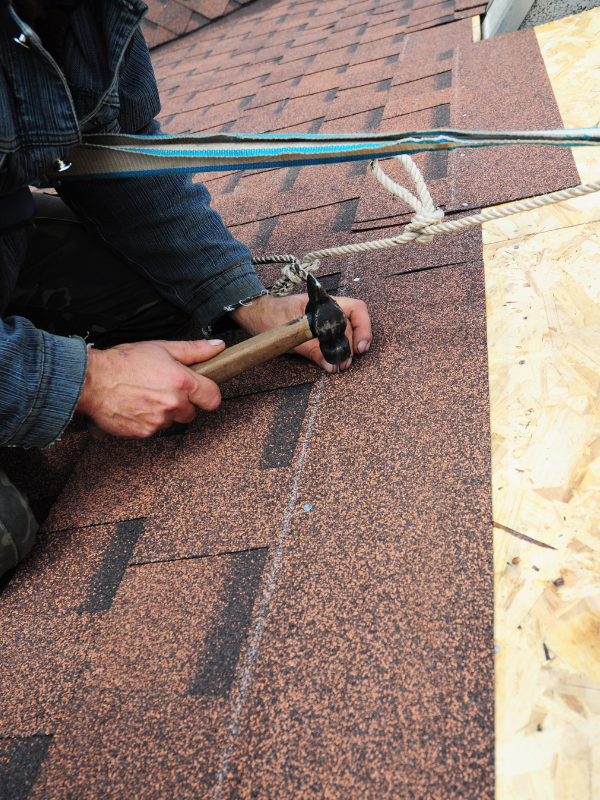 A man is hammering nails into a roof with a hammer.