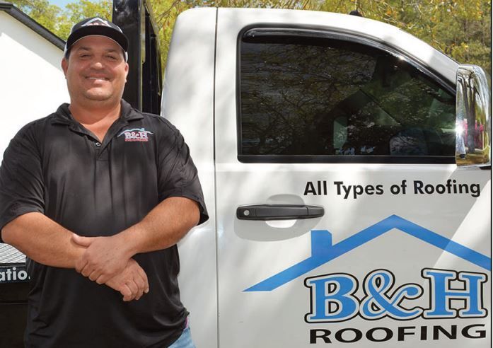 John Harris standing in front of the B & H Roofing truck