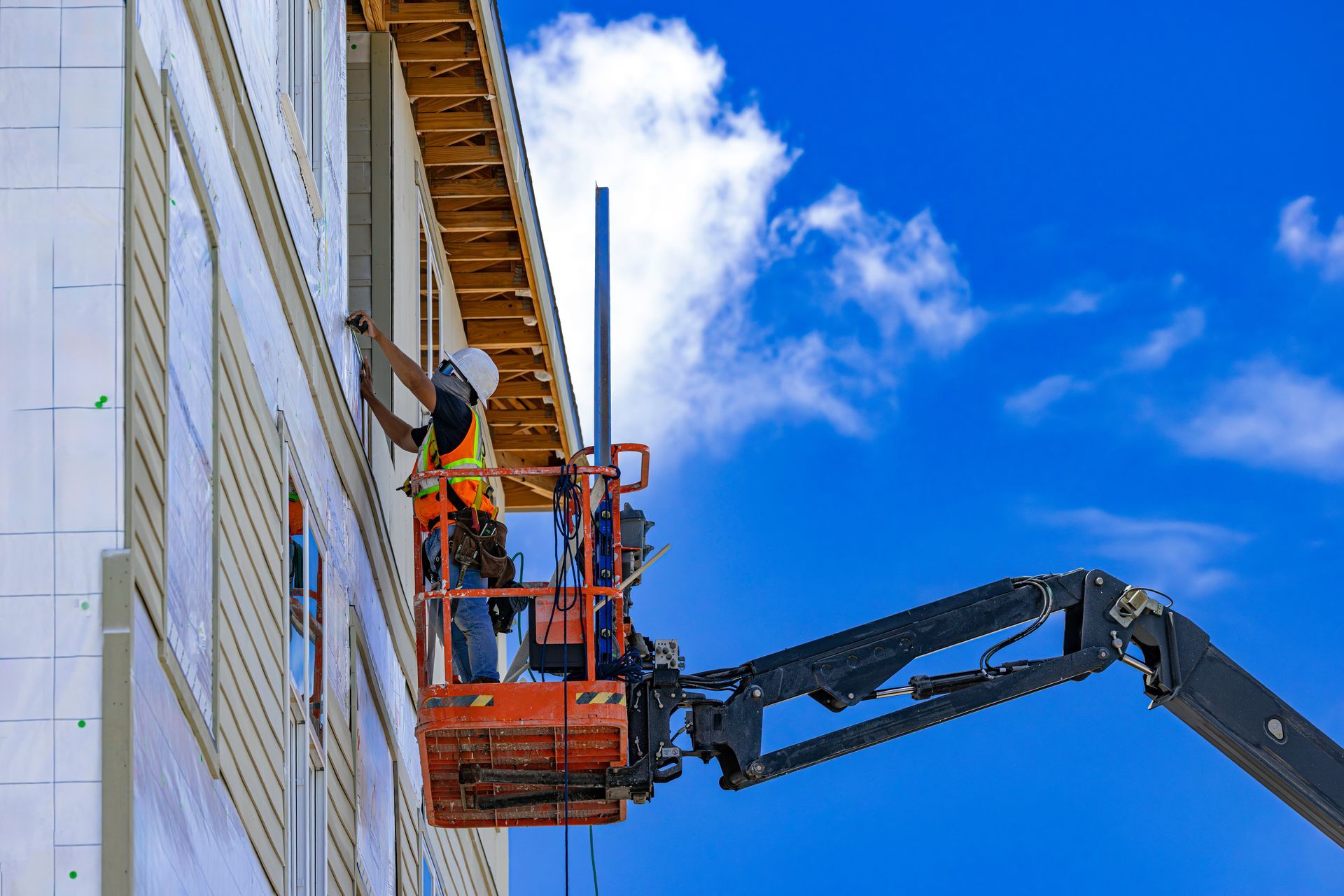 Worker installing siding from an aerial lift on a building under construction
