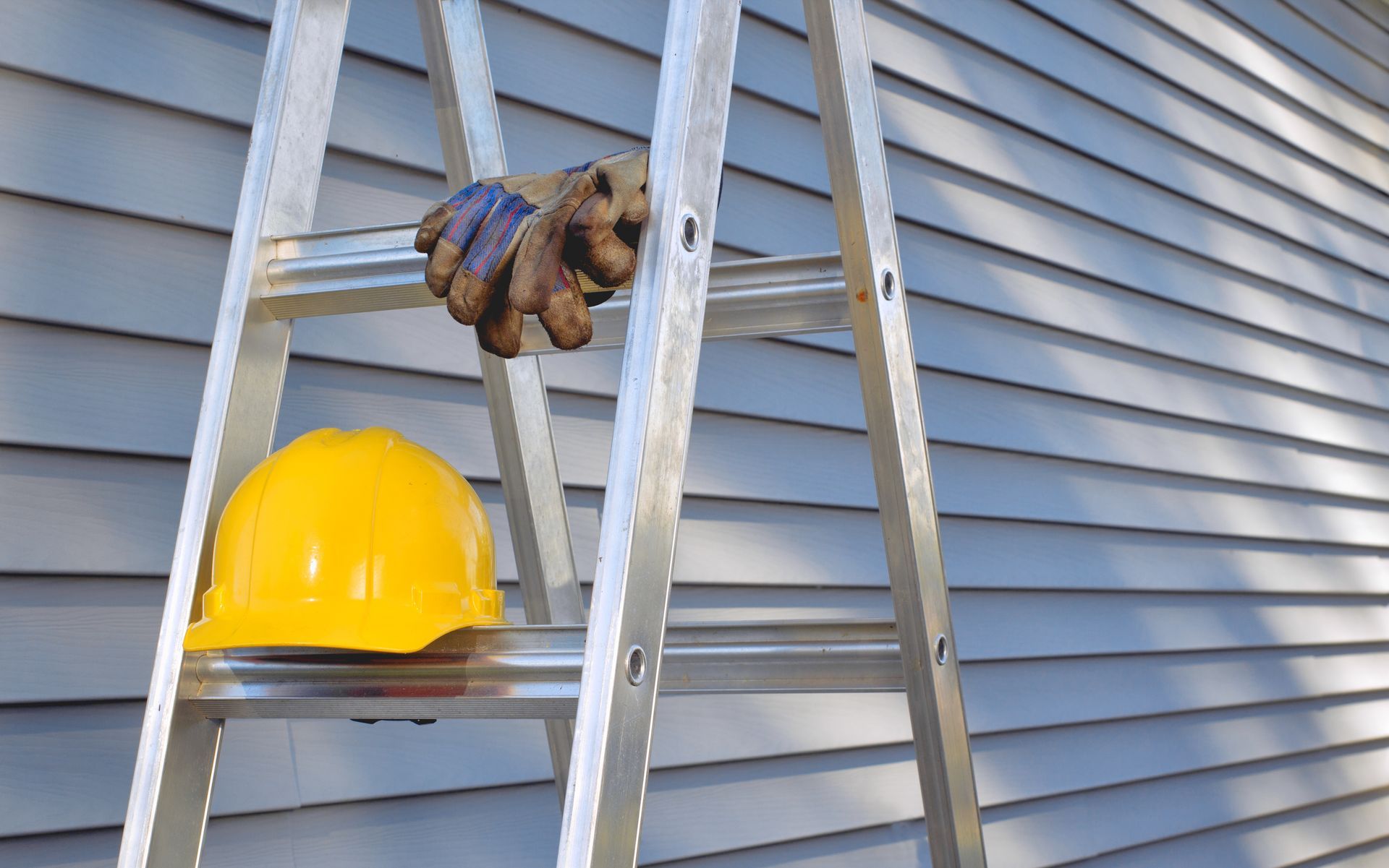 Hard hat and work gloves on a ladder beside house siding