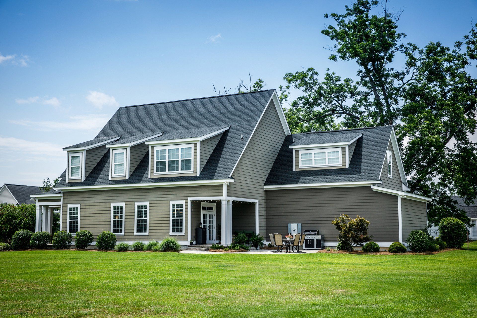 Two-story gray house with dormers, white trim, and a green lawn.