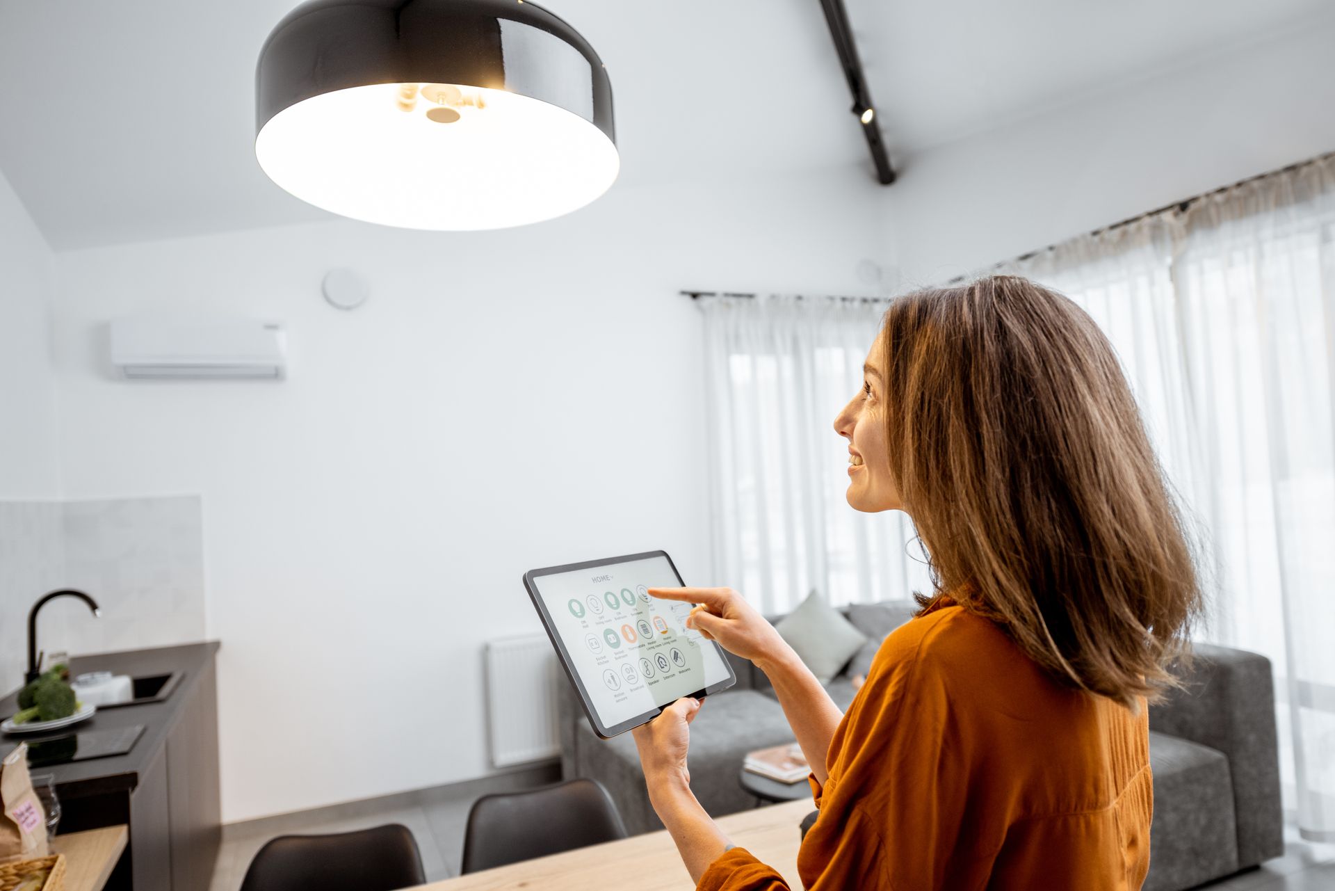 A person in an orange top uses a tablet to control a smart home light fixture in a modern living space. A person in an orange top uses a tablet to control a smart home light fixture in a modern living space.