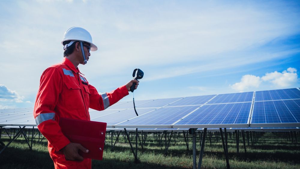 A Man Is Holding A Thermometer In Front Of A Solar Panel — Trusted Energy Solutions In Everton Hills, QLD