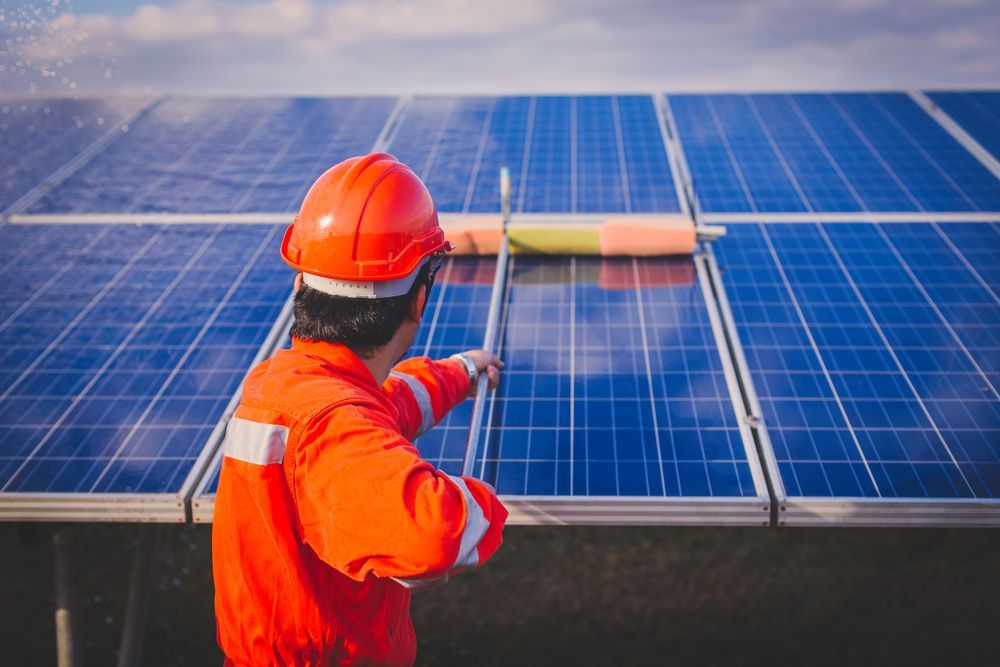 A Man Is Cleaning Solar Panels With A Broom — Trusted Energy Solutions In Labrador, QLD