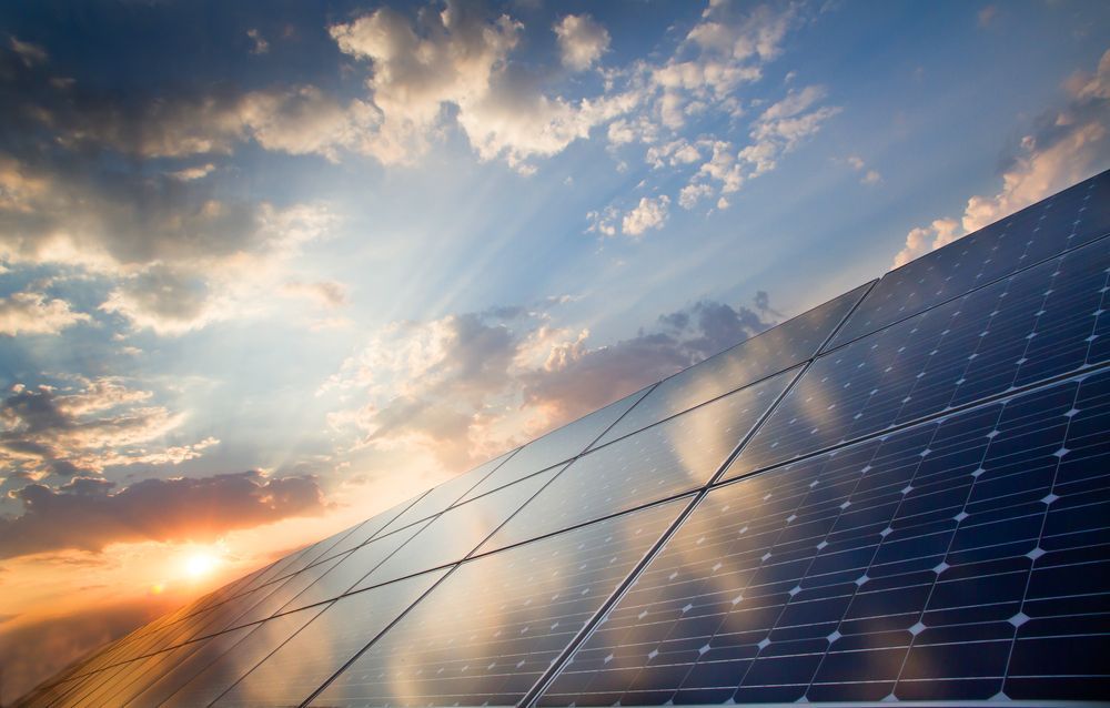 A Row Of Solar Panels Against A Cloudy Sky At Sunset — Trusted Energy Solutions In Ormeau, QLD