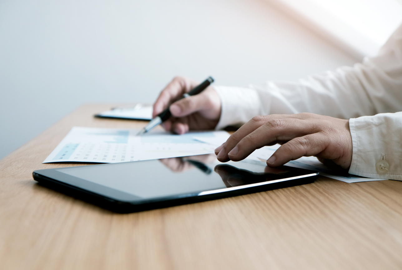 A person is using a tablet and writing on a piece of paper.