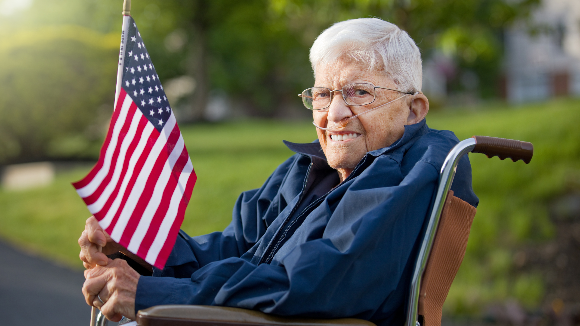 An elderly man in a wheelchair is holding an american flag.