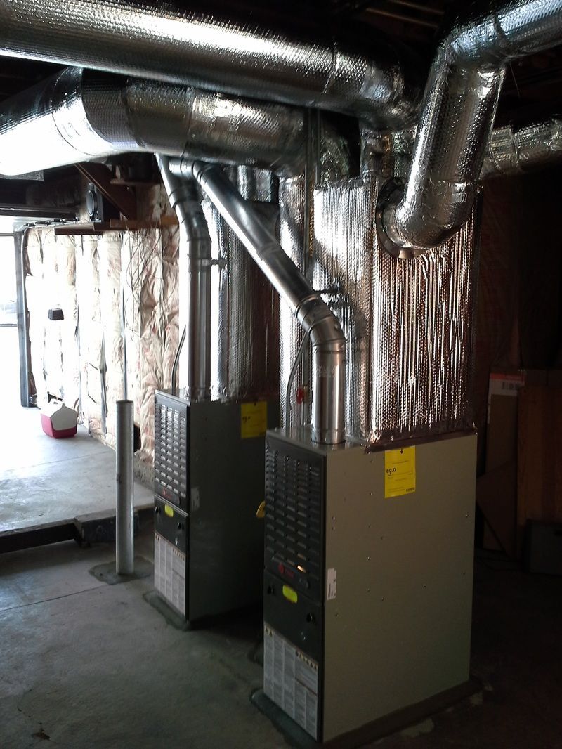 Industrial basement with HVAC units and silver ductwork under exposed pipes