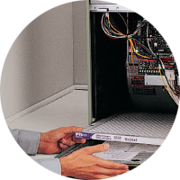Technician opening a server cabinet, holding a manual with exposed cables inside.