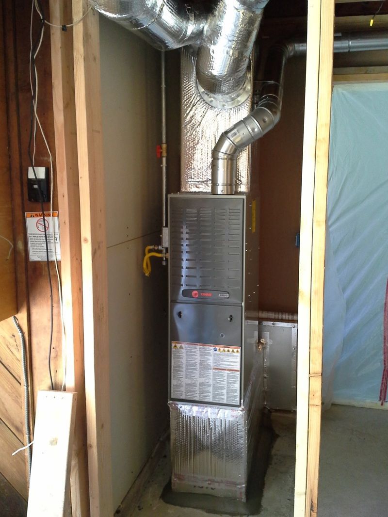 Furnace unit in a narrow utility closet with exposed silver ductwork and unfinished walls
