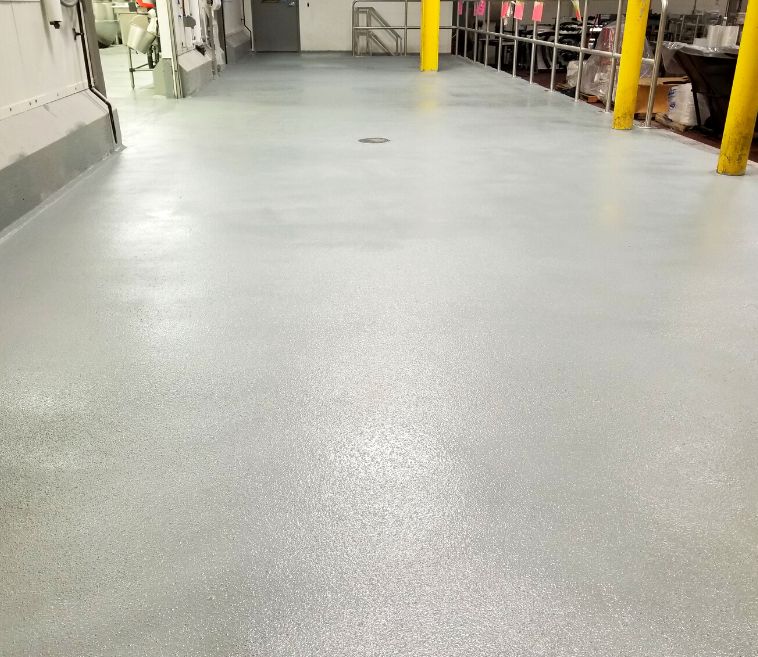 A large empty room with a concrete floor and a wooden wall.