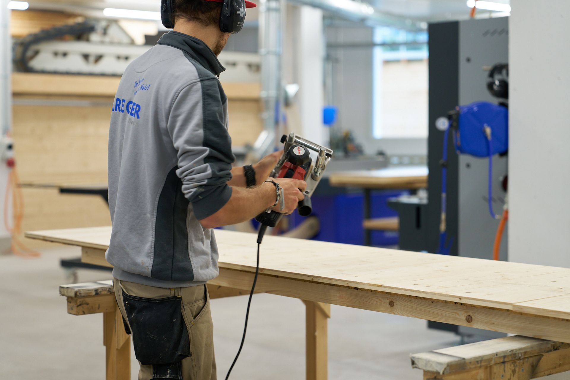 Ein Mann mit Kopfhörern schneidet mit einer Maschine ein Stück Holz.