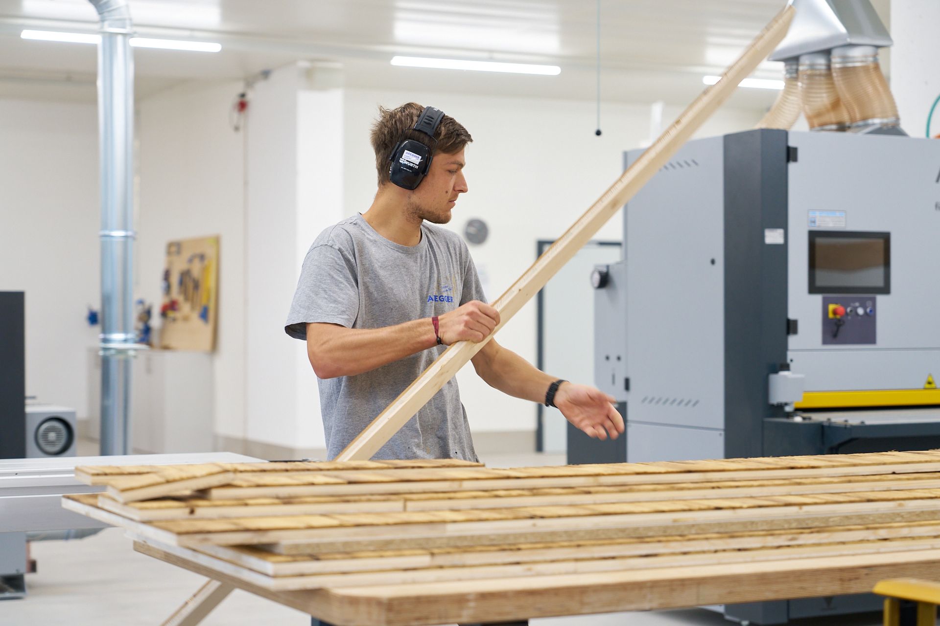 Ein Mann mit Kopfhörern hält in einer Fabrik ein Stück Holz.