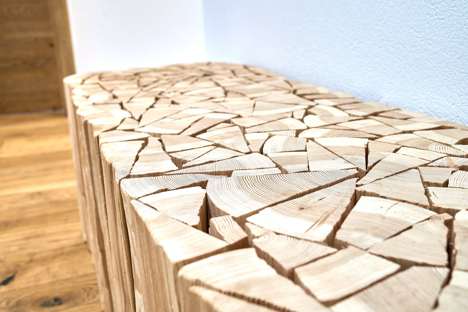 Ein Stück Holz liegt auf einem Holzboden neben einer Wand.