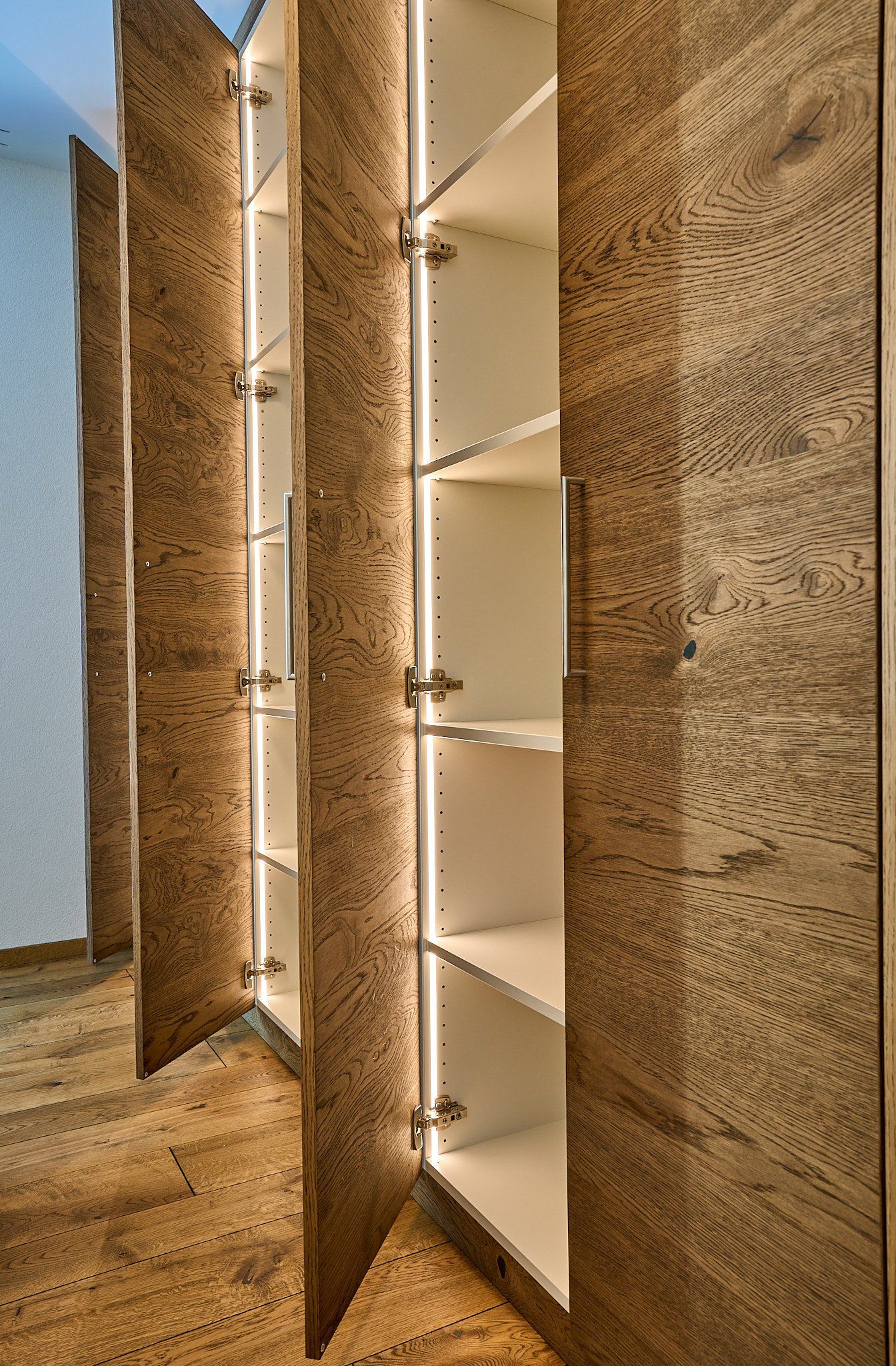 Ein Schrank mit Holztüren und Regalen in einem Flur.