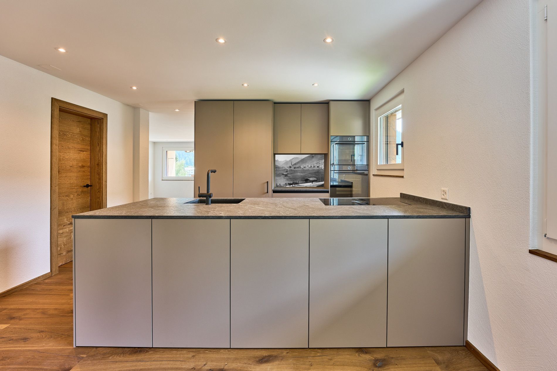 Moderne Küche mit großer Kochinsel, hellen Schränken, Holzboden und Deckeneinbauleuchten