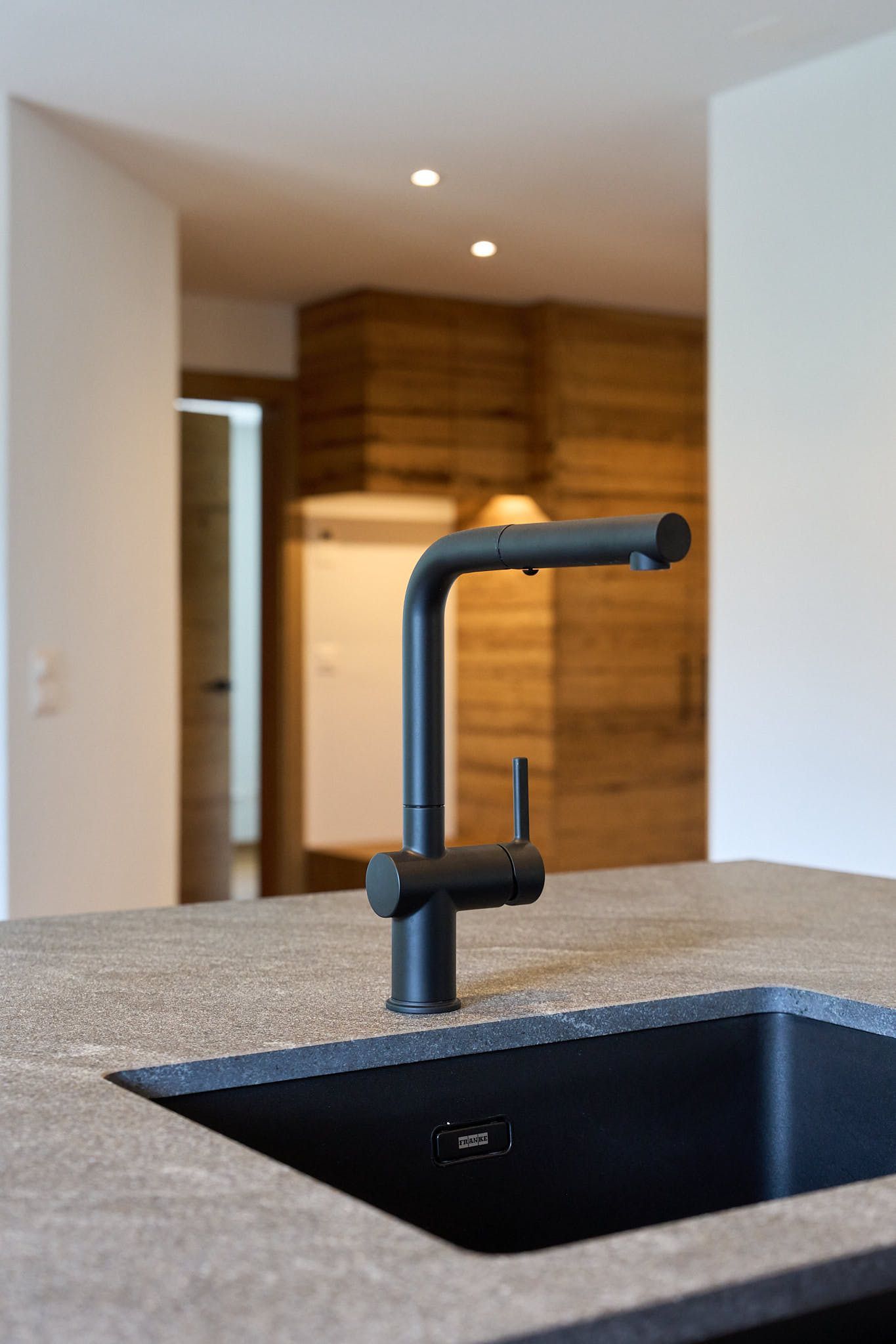 Küchenspüle mit schwarzem Wasserhahn auf einer gesprenkelten Arbeitsplatte, mit Blick auf einen modernen, holzgetäfelten Innenraum.