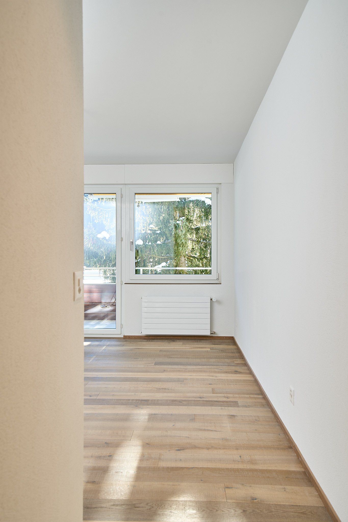 Ein leerer Raum mit Hartholzboden, weißen Wänden und einem Fenster.