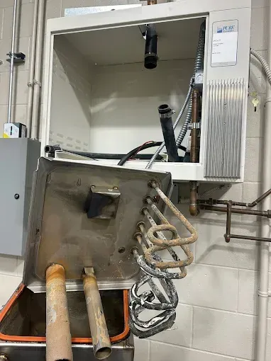 Open wall cabinet with damaged metal panel and exposed pipes in a utility room