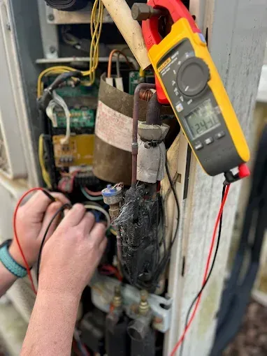 Hands testing electrical wiring with a yellow multimeter in an open equipment panel