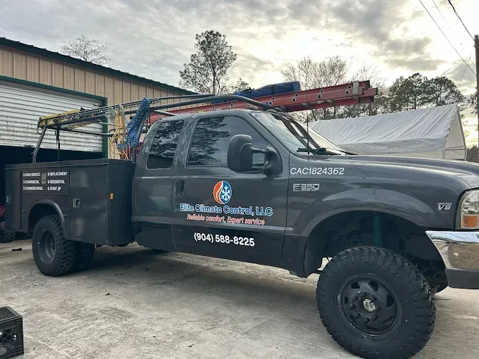 Dark gray service truck with company logo and ladder rack parked beside a building outdoors