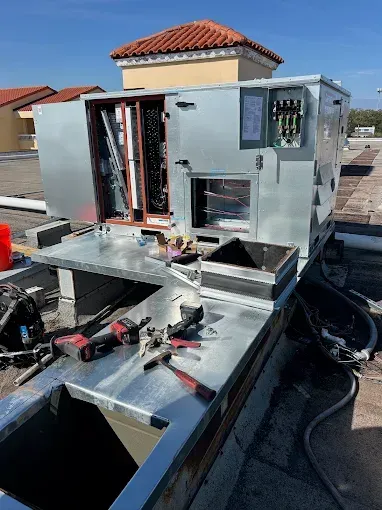 Roof-mounted HVAC unit being repaired, with tools and open panels on a rooftop.
