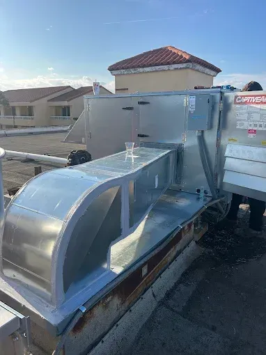 Large silver HVAC unit on a rooftop beside a white utility truck, with houses in the background