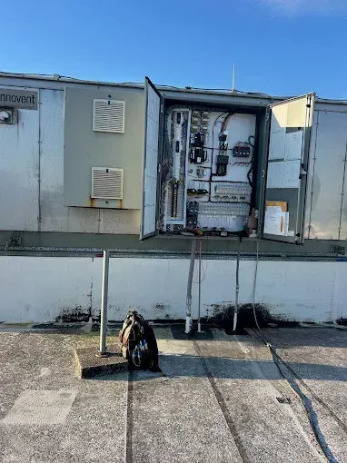 Electrical panel on rooftop with a backpack in front, against a blue sky.