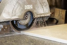 Table saw cutting a white board, with sawdust spraying from the blade