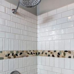 Tiled shower corner with white subway tiles, decorative pebble border, and chrome showerhead.