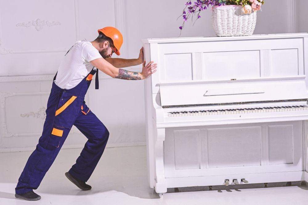 A Man in Overalls and a Hard Hat is Pushing a White Piano — Ocean Grove Removals In Bendigo, VIC