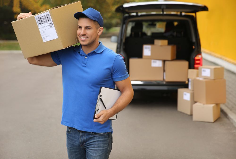 Delivery Man in Blue Uniform Smiling, Carrying a Box — Ocean Grove Removals In Bacchus Marsh, VIC