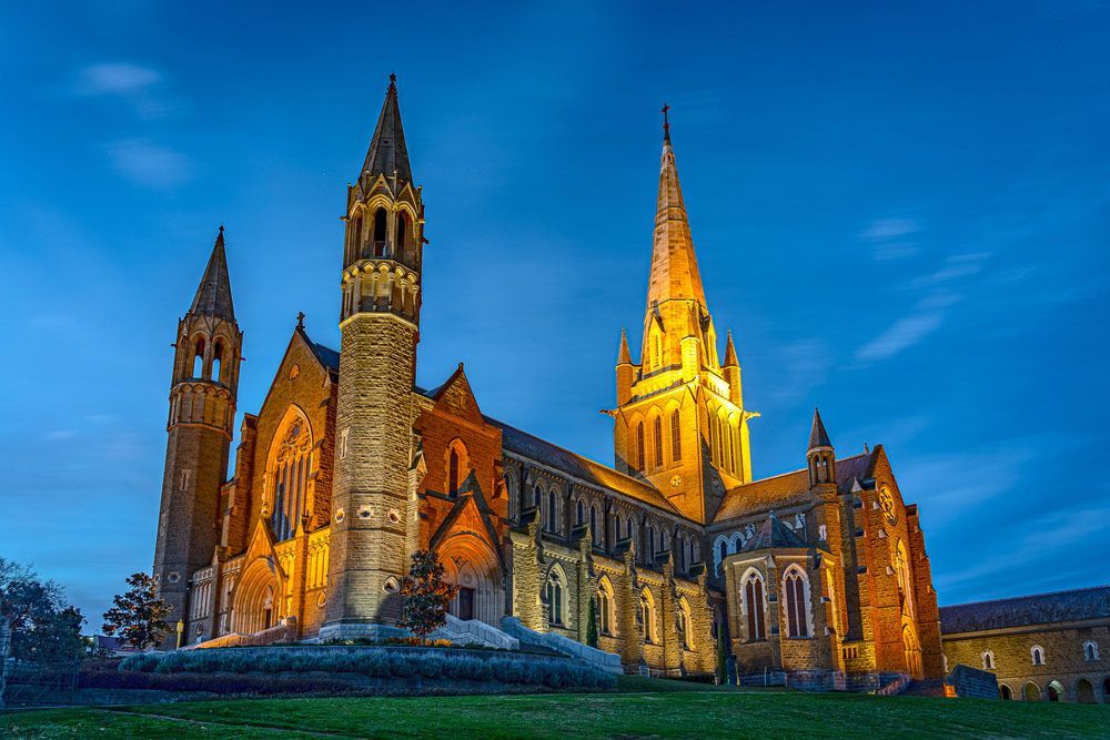 A Large Cathedral is Lit Up at Night With a Blue Sky in the Background — Ocean Grove Removals In Bendigo, VIC