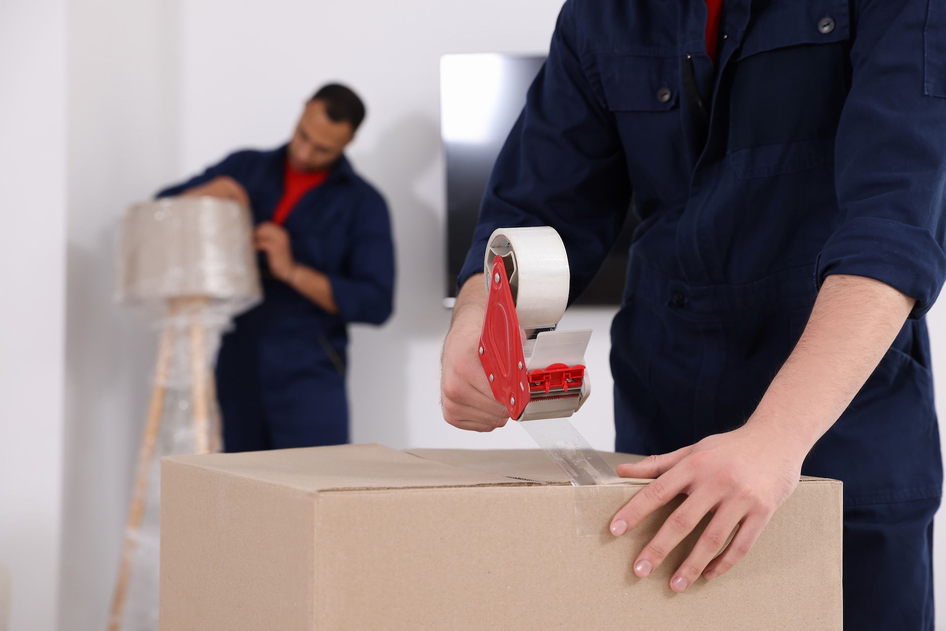 A Man Is Taping a Cardboard Box with Tape — Ocean Grove Removals In Ocean Grove, VIC