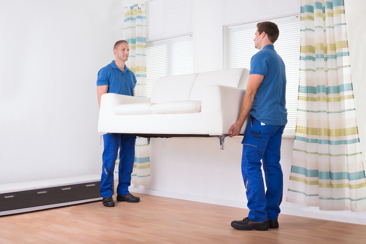 Two Men Are Carrying a White Couch in A Living Room — Ocean Grove Removals In Geelong, VIC