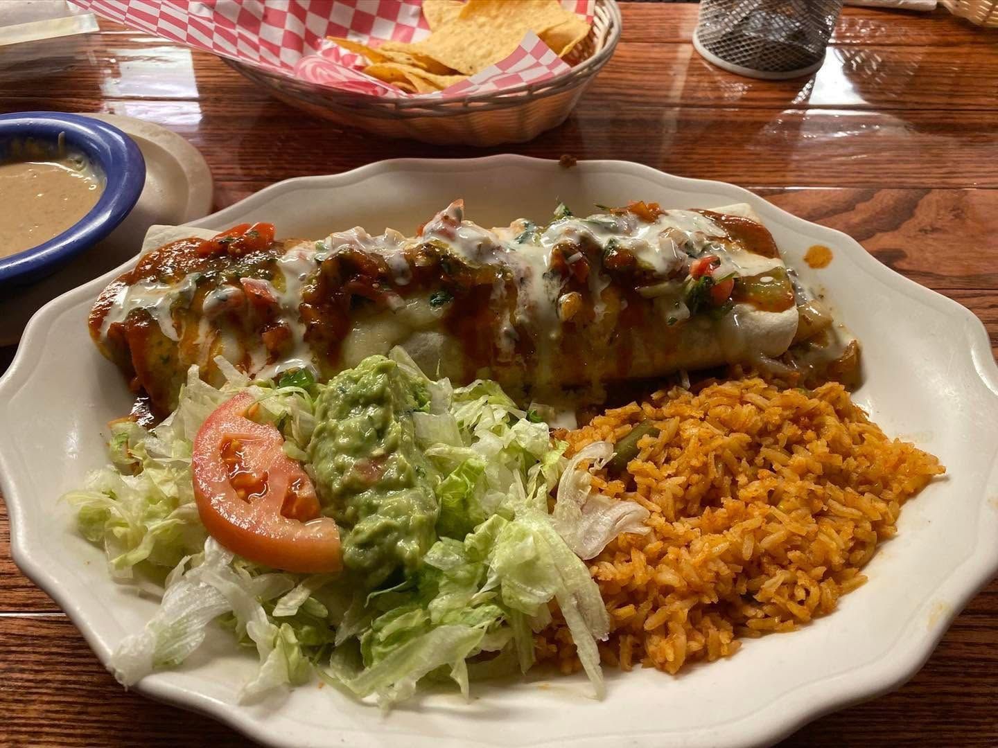 Mexican meal with enchilada, rice, and lettuce-tomato salad on a white plate