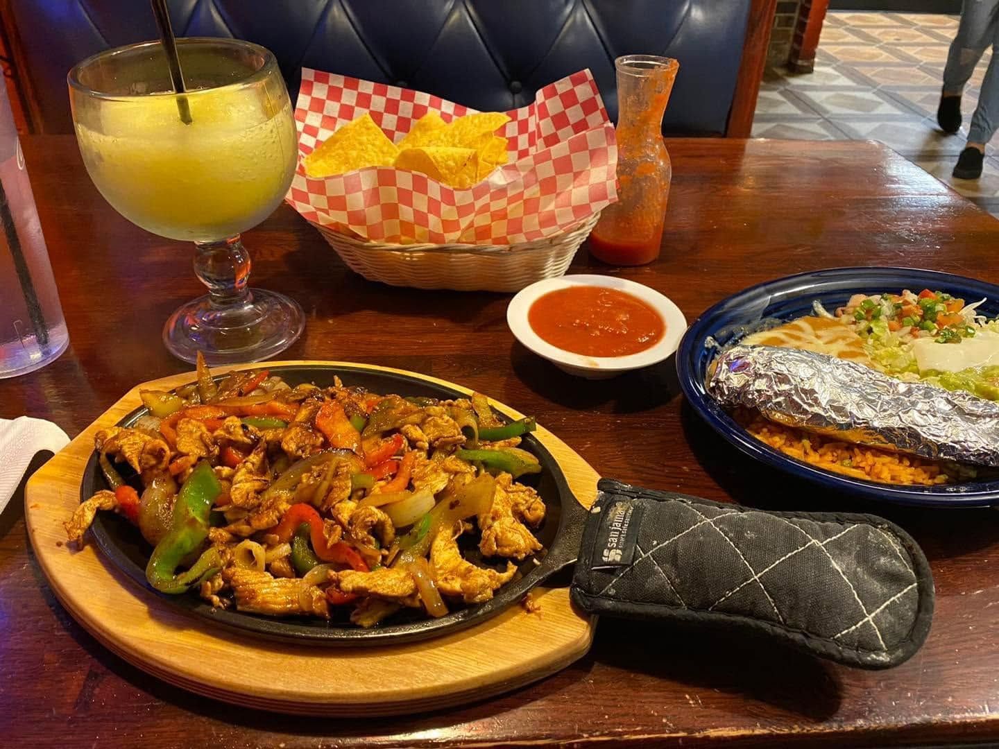 Restaurant table with fajitas, enchiladas, salsa, chips, and a margarita