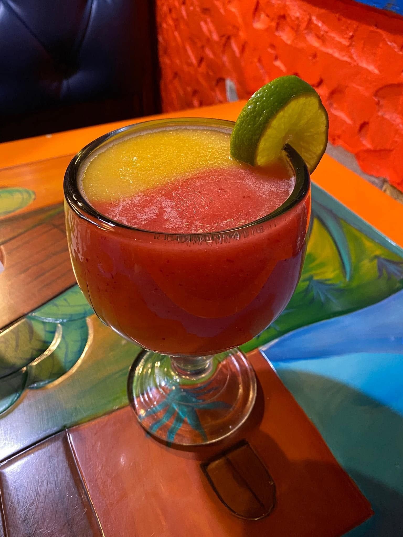 Colorful frozen cocktail in a stemmed glass with a lime garnish on a bar table