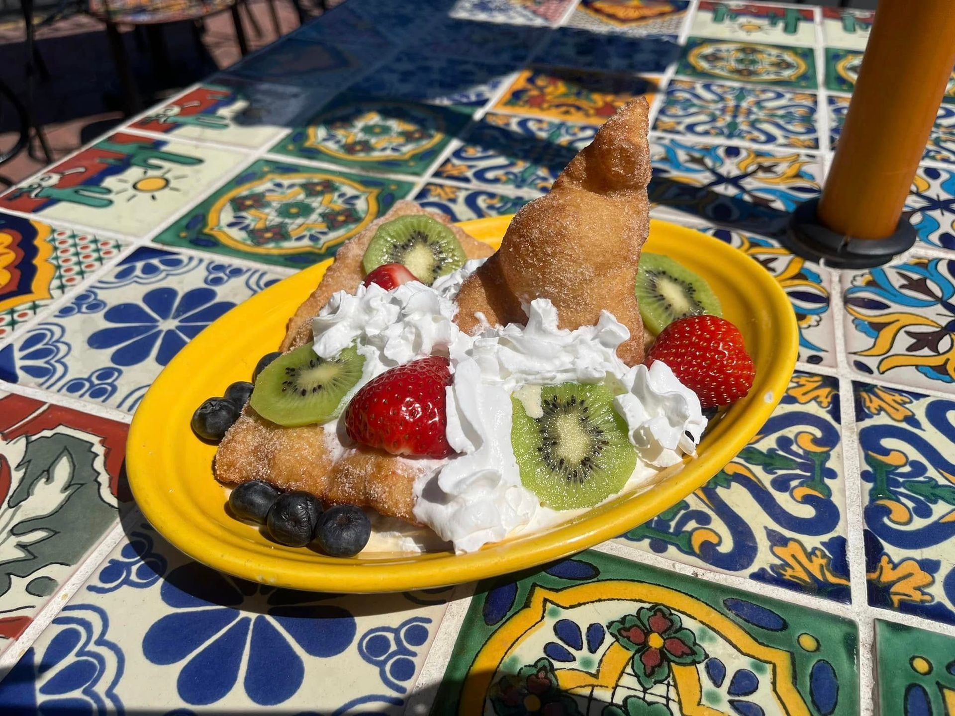 Dessert plate with waffles, whipped cream, berries, kiwi, and a cone on a colorful tiled table