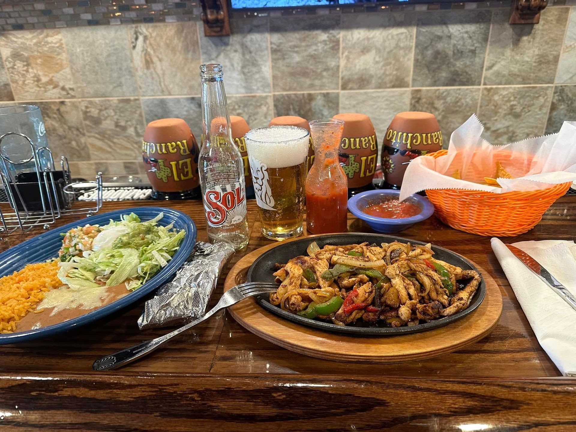 Mexican meal spread with tacos, rice, salad, salsa, and drinks on a wooden table