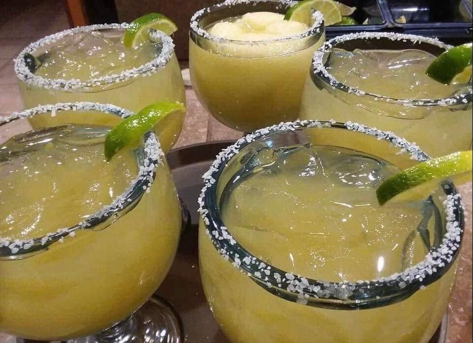 Five salt-rimmed margaritas with lime wedges on a table