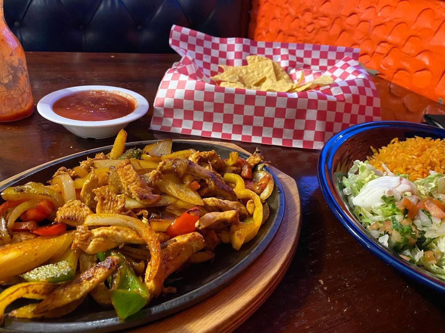 Plate of sizzling stir-fried noodles and vegetables with sauce, chips, and a salad on a restaurant table